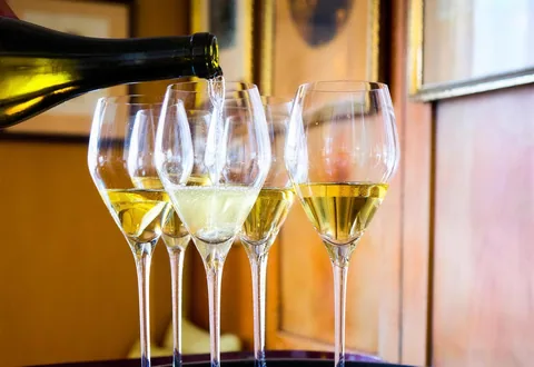 Champagner wird in vier Gläser eingeschenkt