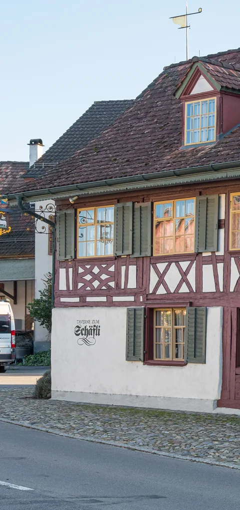 Das Riegelhaus der Taverne zum Schäfli mit dem gemalten Namen an der Wand und dem Wirtshausschild