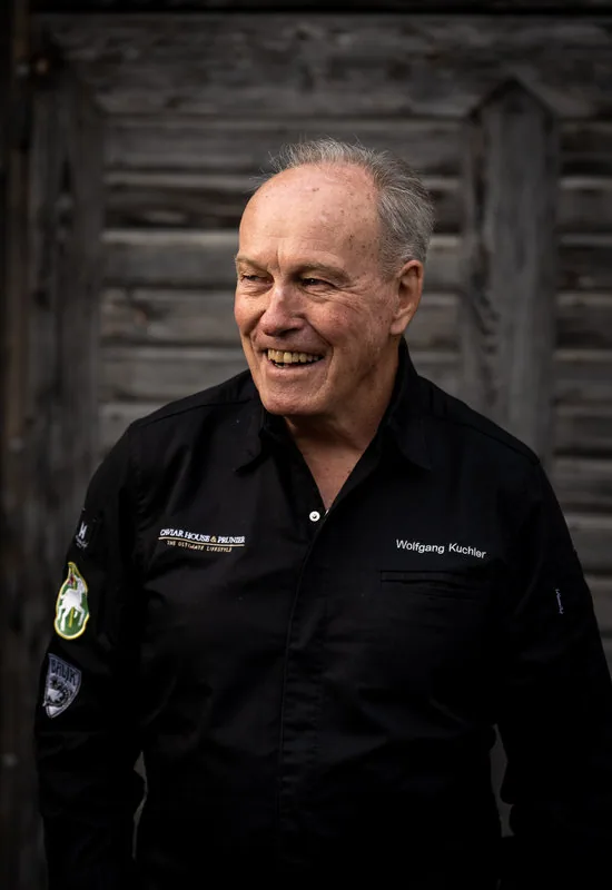 Wolfgang Kuchler in der Kochjacke vor der alten Holzwand