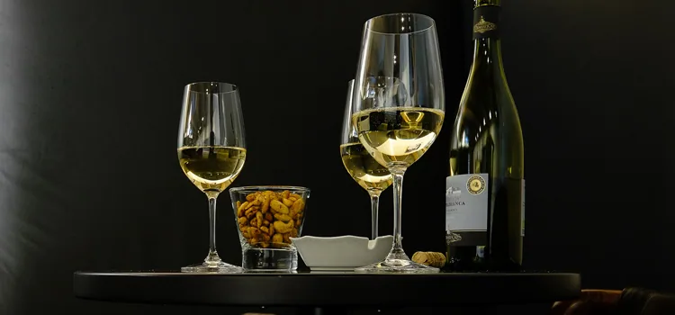 Weissweingläser, eine Flasche und Nüsse auf dem dunklen Tisch