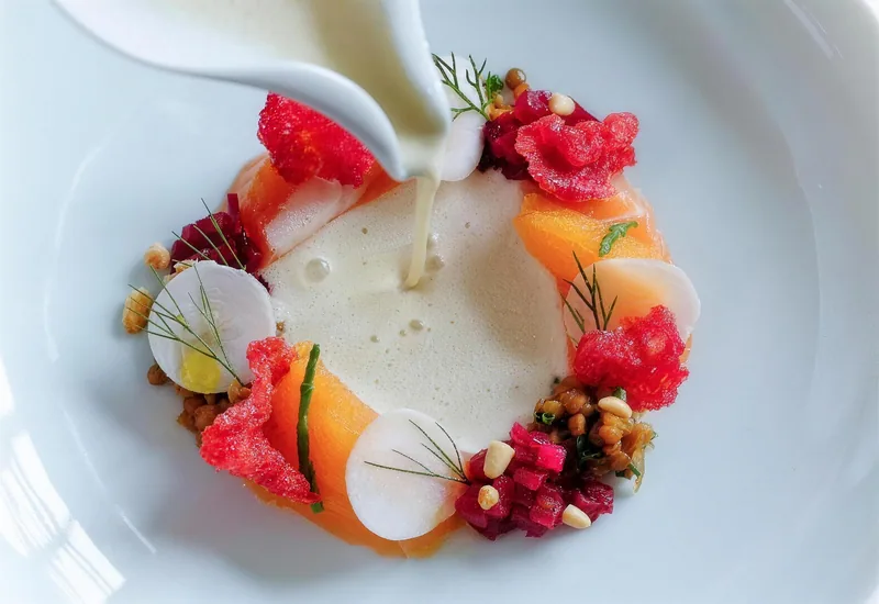 Ein Teller mit Gemüse und Beeren im Kreis, die Sauce wird angegossen