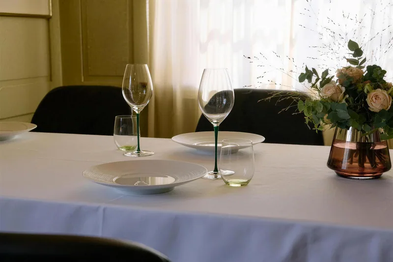 Ein gedeckter Tisch mit Weingläsern und Blumen am Fenster