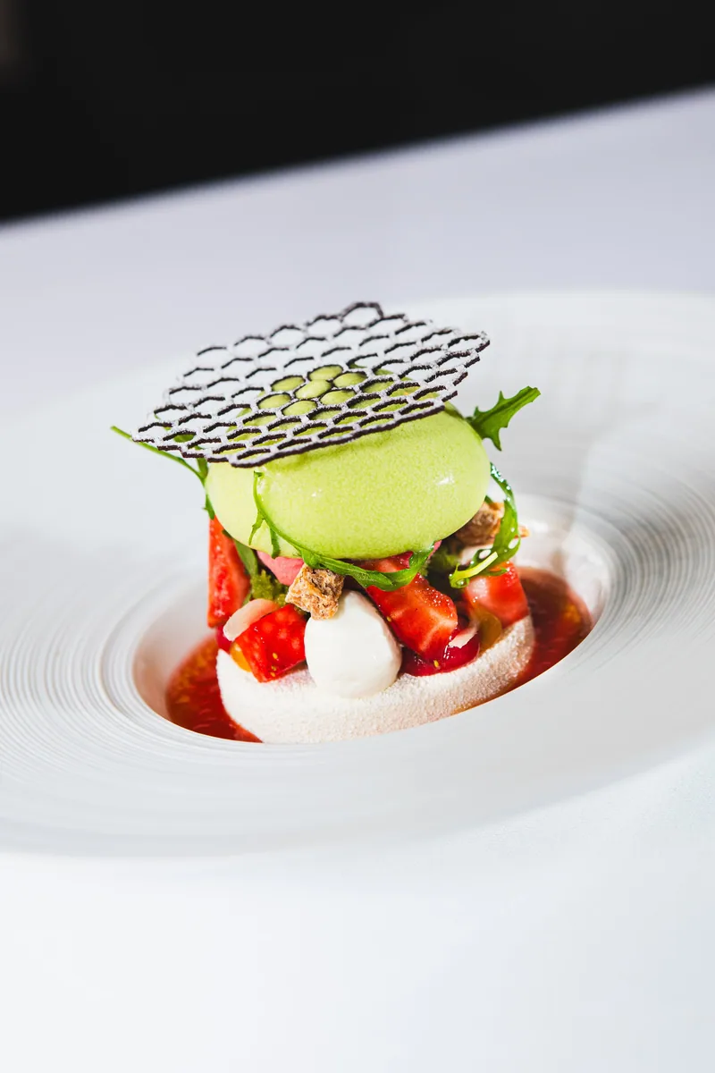Ein Dessert mit Erdbeeren, einer grünen Kugel und einem Gitter aus Zucker